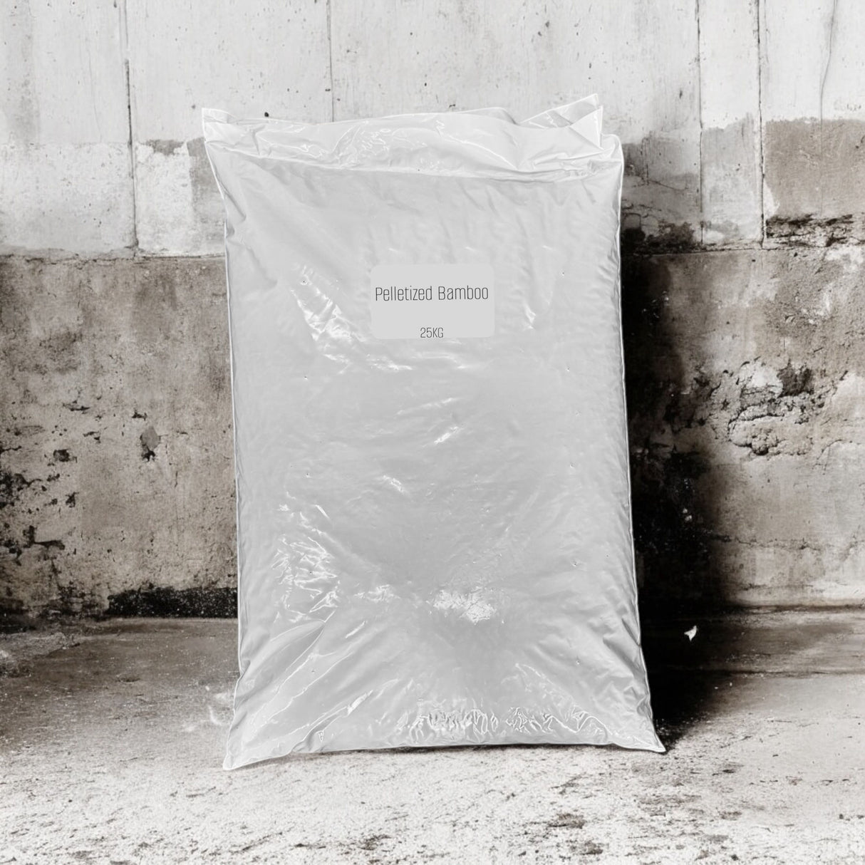 A large white plastic bag labeled 'Pelleted Bamboo' and '25KG' standing upright against a weathered concrete wall and floor.