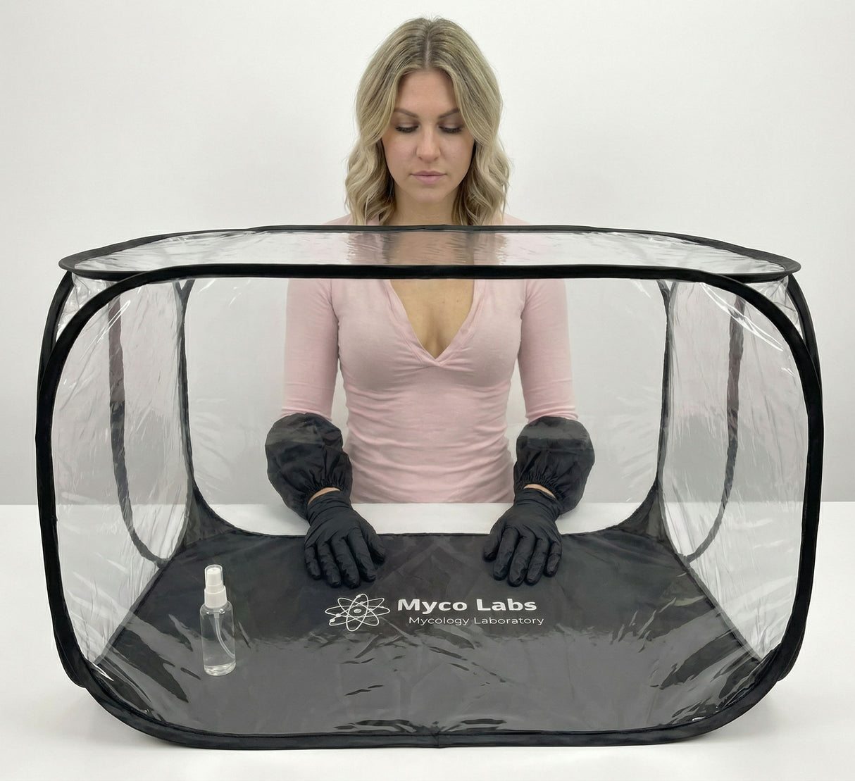 Person wearing black gloves and a pink shirt inside a transparent Myco Labs tent on a white background
