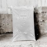 A large white plastic bag labeled 'Pelleted Bamboo' and '25KG' standing upright against a weathered concrete wall and floor.