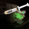 Myco Labs Ghost Fungus (Omphalotus nidiformis) liquid culture syringe, 10cc, with ghost fungus caps behind it in the dark