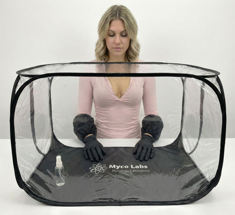 Person wearing black gloves and a pink shirt inside a transparent Myco Labs tent on a white background